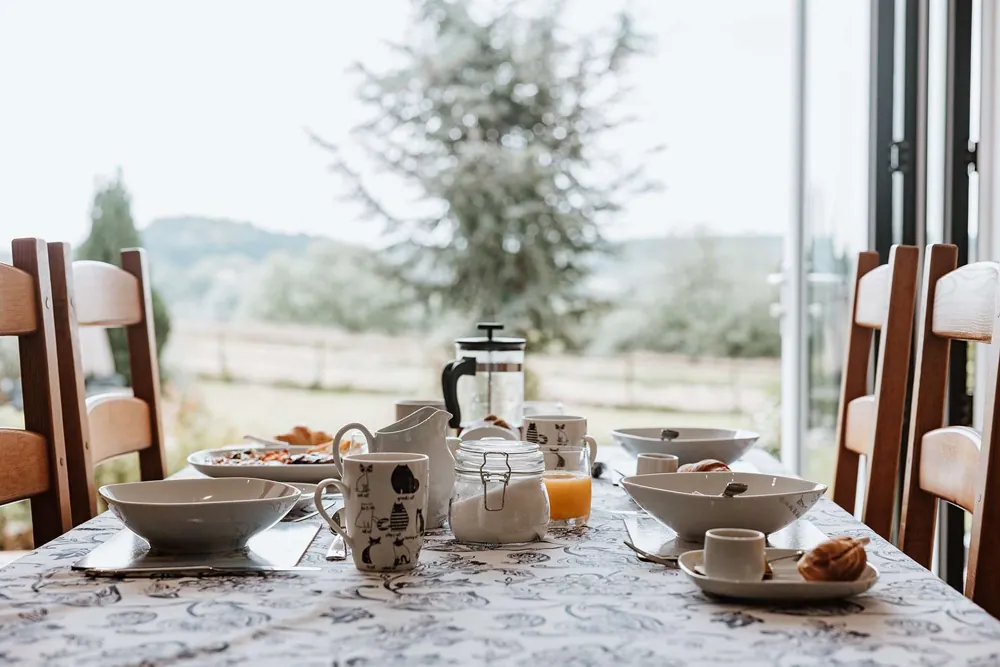 Breakfast laid at the table by open glass doors, fields rolling away beyond the garden