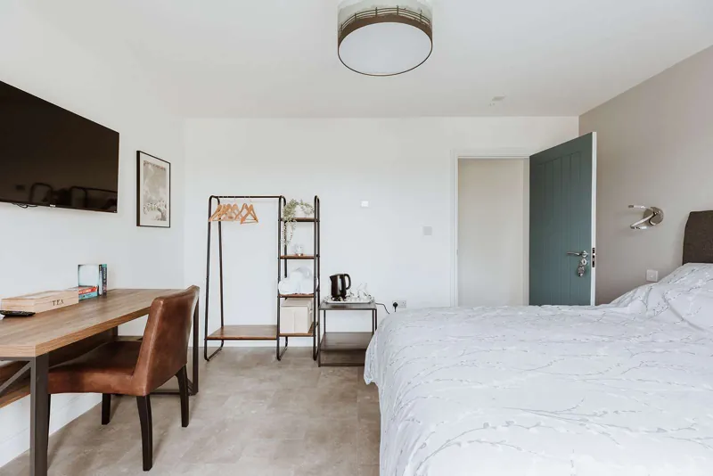 The Bridge Room: crisp white king bed beside a leather desk chair and iron-framed shelving