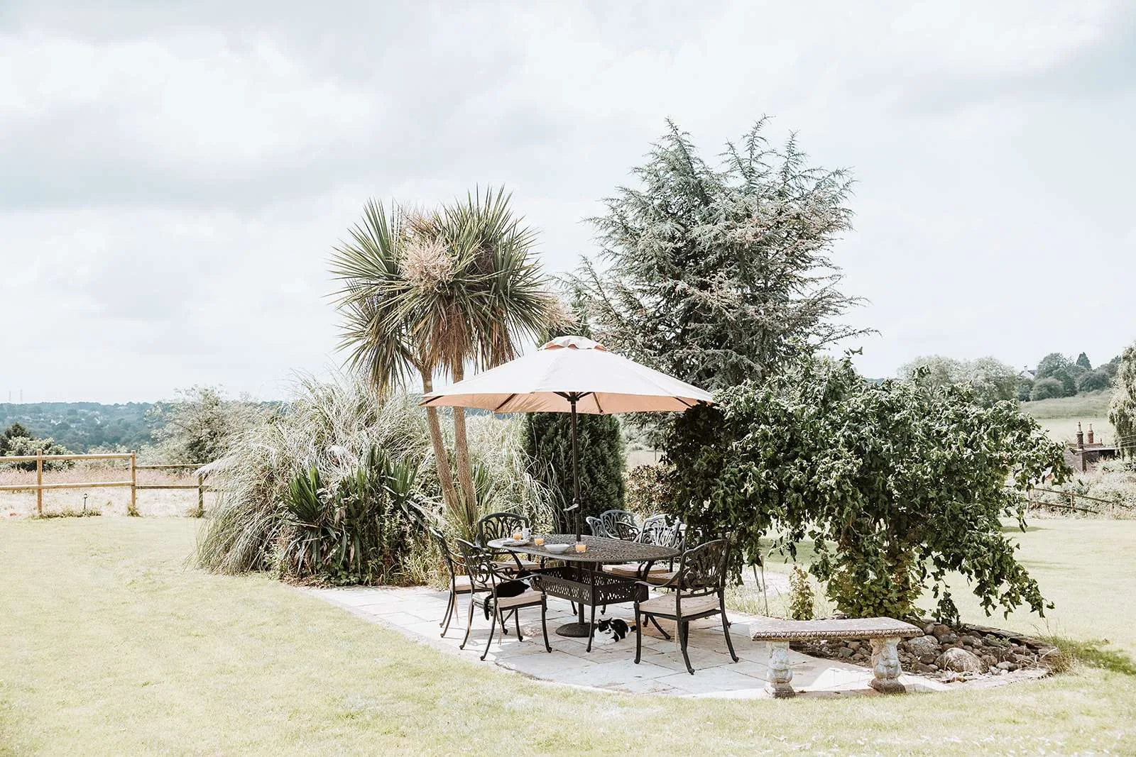 The garden at The Woodlands: a parasol and table on the mown lawn, mature trees and borders, and open Shropshire countryside running to the horizon
